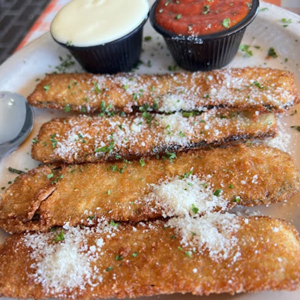 Four golden-brown fried zucchini sticks topped with parmesan cheese and parsley, served with marinara and white sauce.