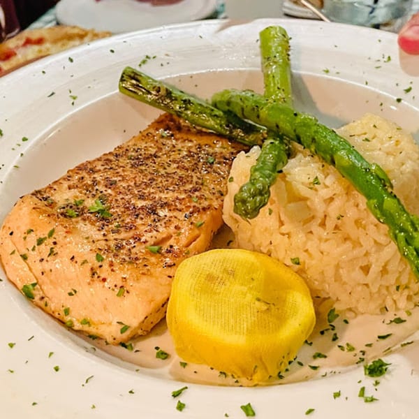 Grilled salmon with asparagus, rice pilaf, and a lemon wedge on a white plate at Gabriella's.