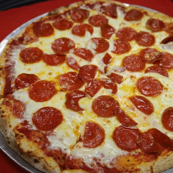 A close-up of a whole pepperoni pizza from Gabriella's, with melted cheese and a red background.