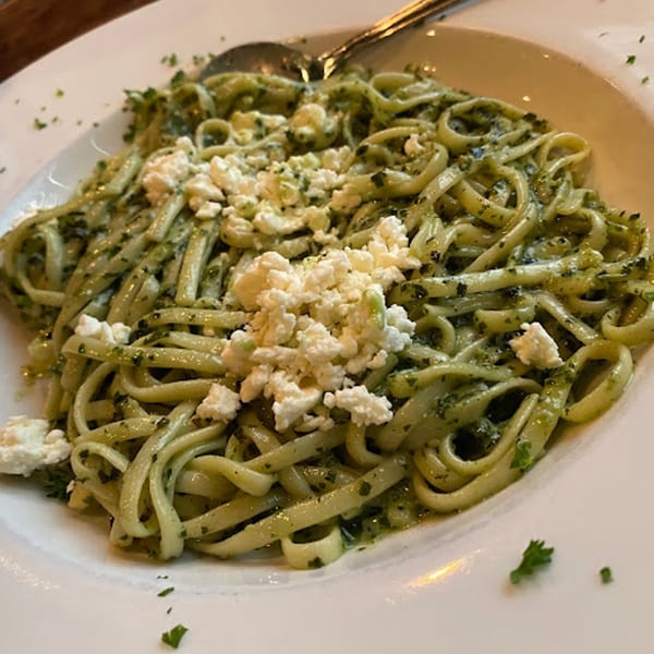 Gabriella's linguine pasta with pesto sauce and crumbled feta cheese on a white plate.
