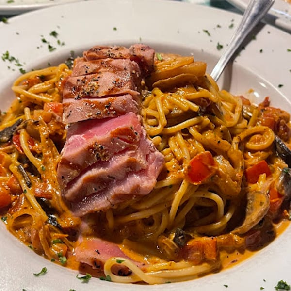 Seared tuna slices on a bed of spaghetti with creamy tomato sauce, mushrooms, and red peppers.